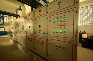 Large industrial control panel with multiple switches, lights, and meters in a mechanical room