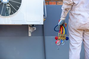Technician holding HVAC manifold gauges near an outdoor air conditioning unit