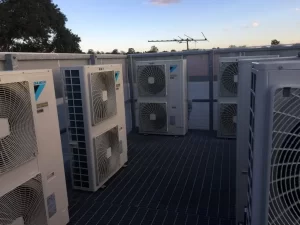Multiple Daikin outdoor air conditioning units installed on a rooftop platform with metal grating and fencing.