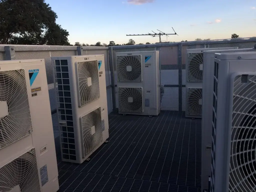 Multiple Daikin outdoor air conditioning units installed on a rooftop platform with metal grating and fencing.